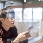 窓辺でスマートフォンを持つ男性